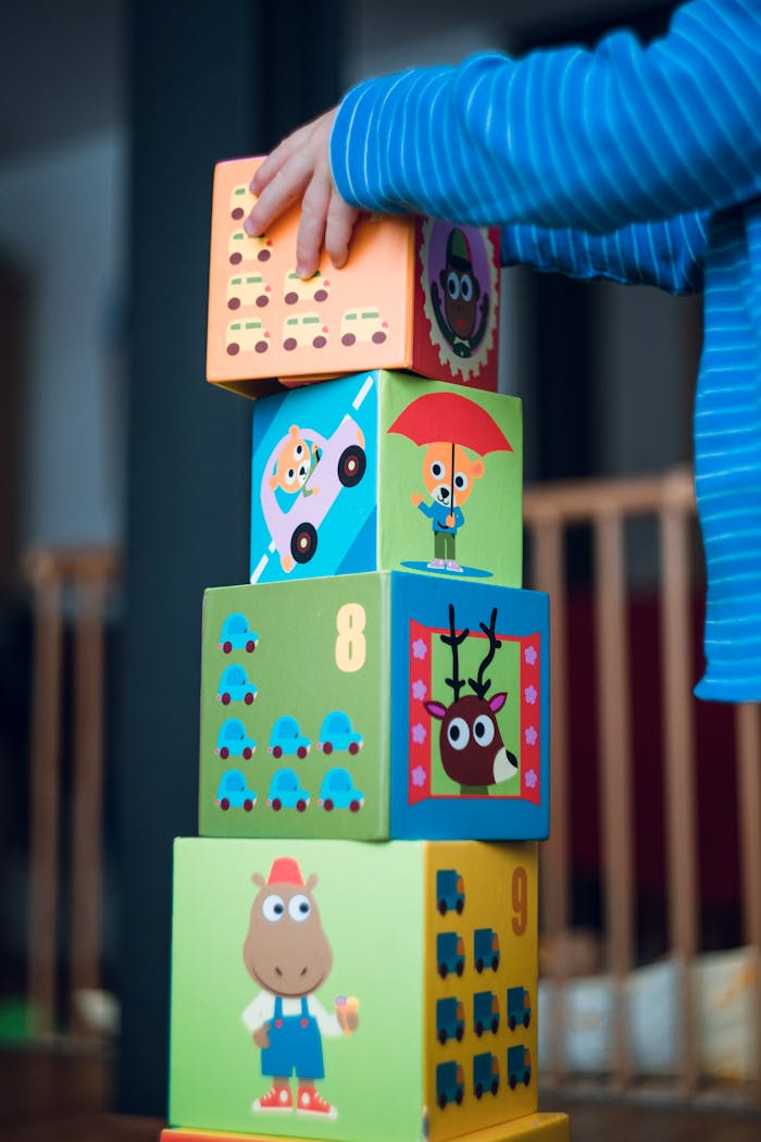 impact-img A child playing indoors, stacking colorful wooden toy blocks with joyful illustrations.