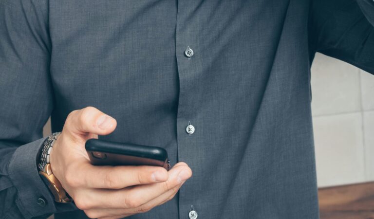 A stressed man looks at his smartphone, holding a credit card in his hand.
